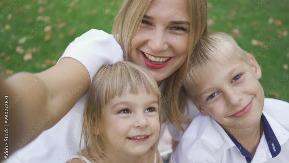 Young caucasian woman and two children taking selfie in the park. Mother with kids laughing. Mom talking to her kids. Family having fun outdoors. Young caucasian woman and two children taking selfie in the park. Mother with kids laughing. Mom talking to her kids. Family having fun outdoors.