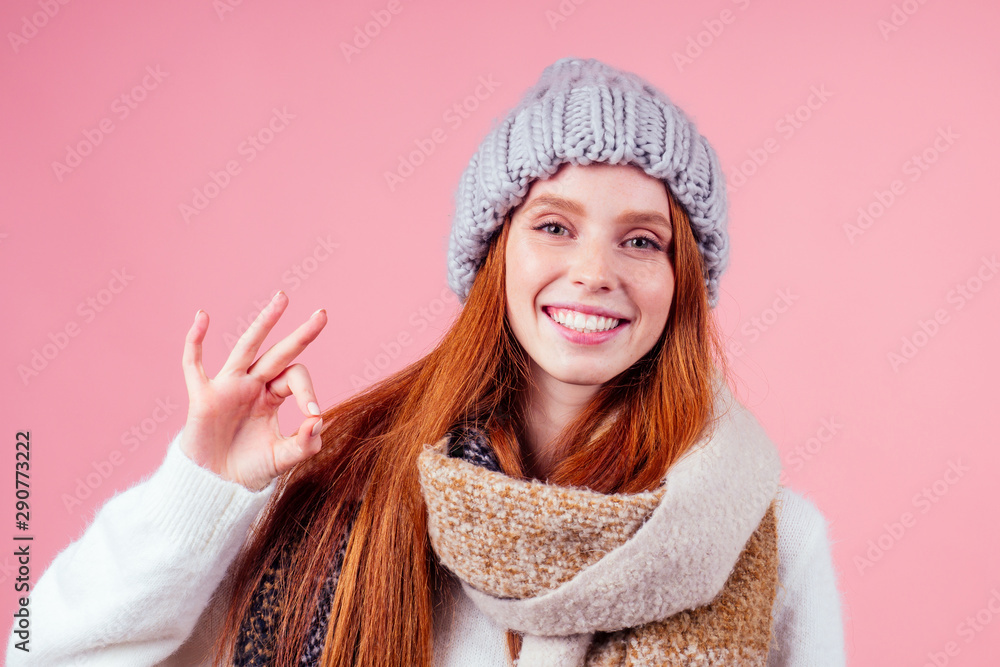 redhaired ginger woman wear stylish wool hat ,sweater and scarf looking at camera and pointing fingers okay at copyspase in studio pink background redhaired ginger woman wear stylish wool hat ,sweater and scarf looking at camera and pointing fingers okay at copyspase in studio pink background