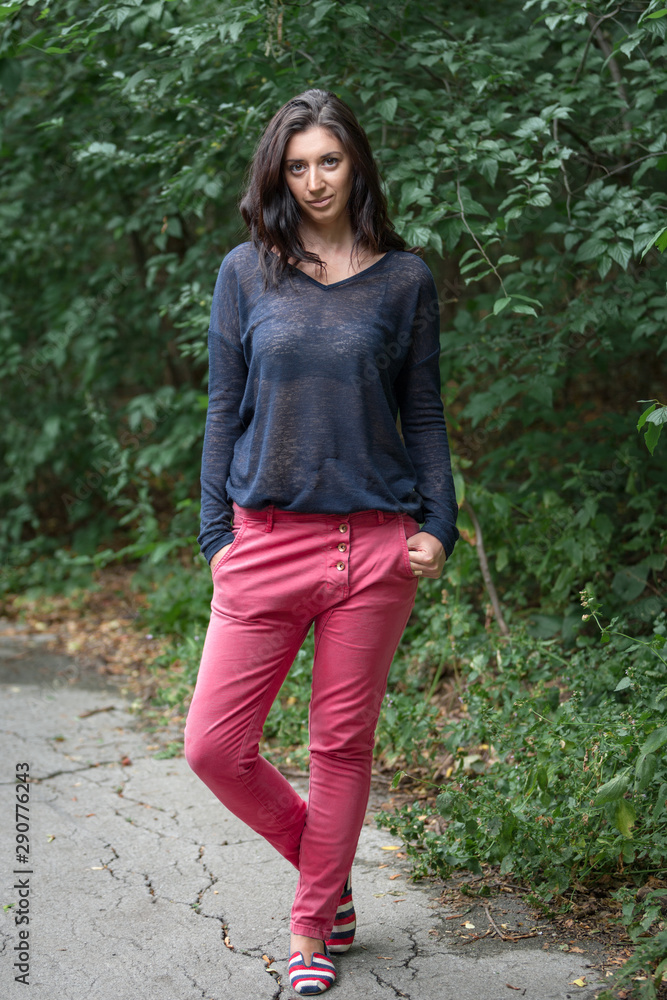 Beautiful brunette on a background of foliage. She folded her hands in her pockets. In full growth. Beautiful brunette on a background of foliage. She folded her hands in her pockets. In full growth.