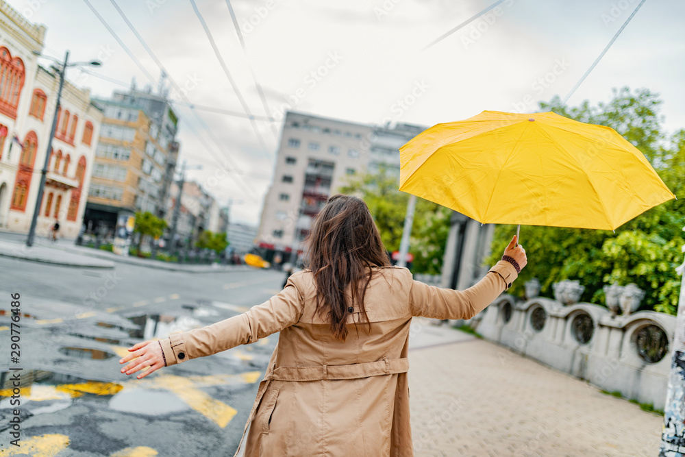 Fototapeta premium Joyful woman walking in rainy weather. Happy young woman walking with umbrella under the rain. I love it when it's raining! This weather won't get me down