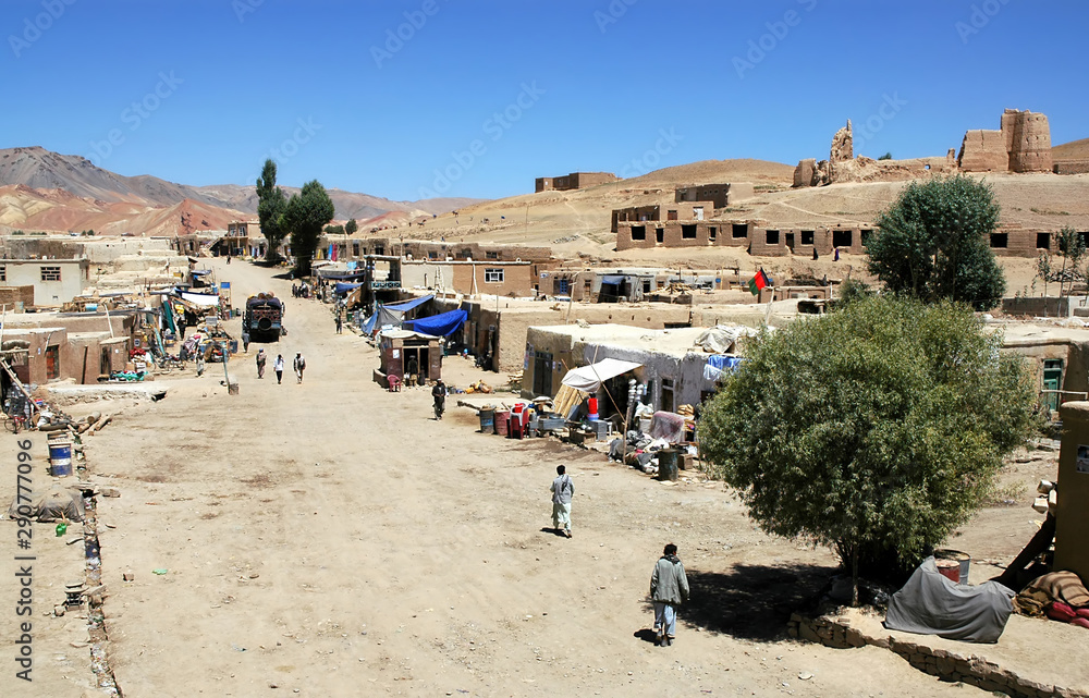 Lal Wa Sarjangal, Ghor Province in Central Afghanistan. This is the dusty main street in Lal. The low basic buildings and dirt road are typical in remote towns in Afghanistan. Note the Afghan flag.