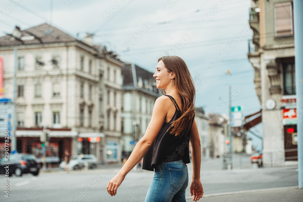 Outdoor portrait of beautiful young woman walking down the road in the city, wearing black cami top and denim jeans. Image taken in Lausanne downtown, Switzerland