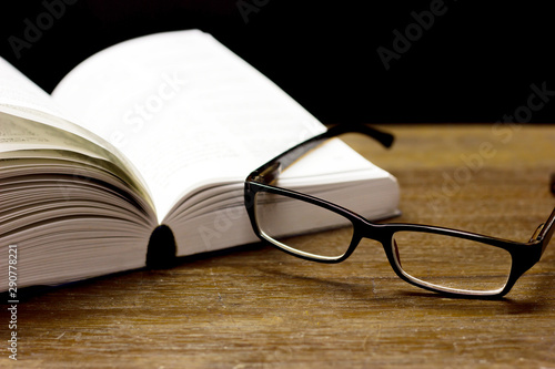 Open books and place eyeglasses on the old wooden desk.