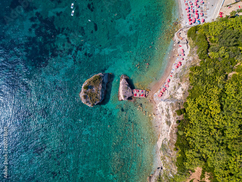 Aerial view of Sveti Nicola, Budva island, Montenegro. Hawaii beach, umbrellas and bathers and crystal clear waters. Jagged coasts