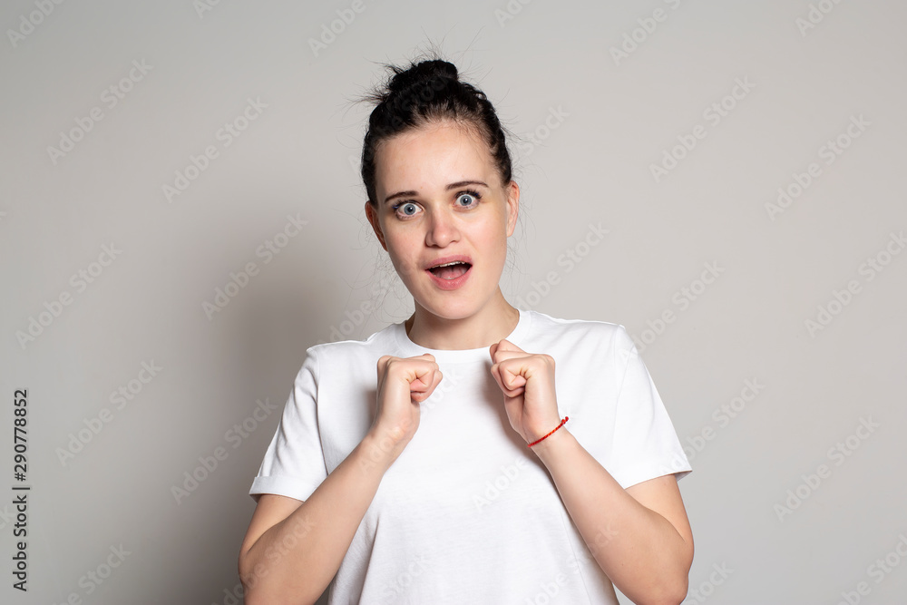 Young woman in anticipation of a surprise emotionally and excitedly clenched her hands into fists, and looks into the camera with wide open eyes and mouth. Young woman in anticipation of a surprise emotionally and excitedly clenched her hands into fists, and looks into the camera with wide open eyes and mouth.