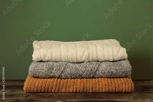 Bunch of knitted pastel color sweaters with different knitting patterns perfectly folded in stack on brown wooden table, green textured background. Fall winter season knitwear. Close up, copy space. © Evrymmnt