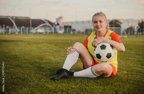 Portrait of teen girl football player with soccer ball sitting on the grass, copy space