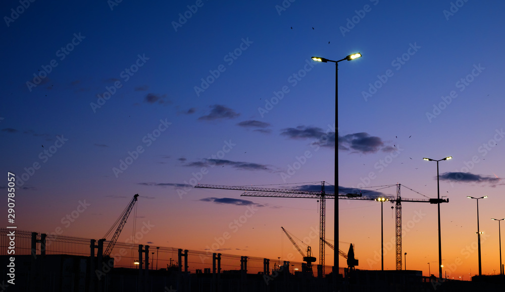 Silhouettes of cranes in the harbor at sunset