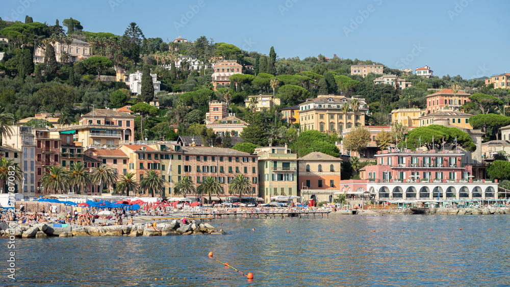 Santa Margherita, Genoa, Italy. View of the marine town. In the background the green Ligurian mountains with historic buildings. In the foreground, the Ligurian Sea with tourists on the beach