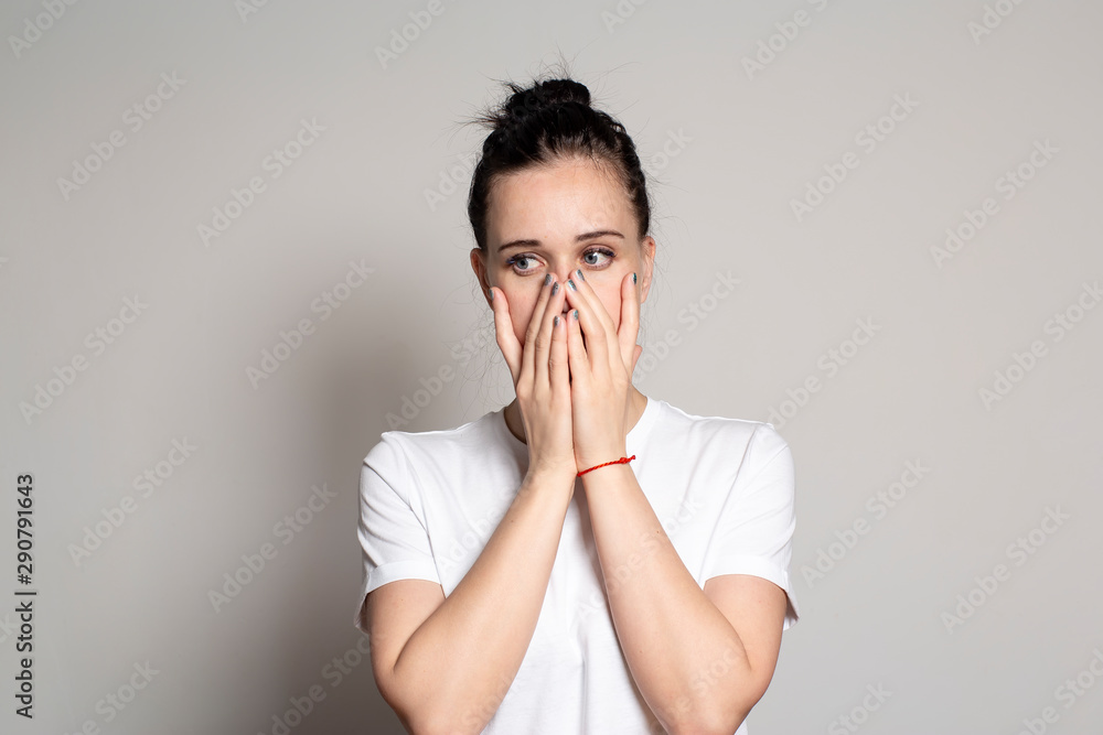 A shocked young woman closed her mouth with both hands and looks away. Isolated on a white background. A shocked young woman closed her mouth with both hands and looks away. Isolated on a white background.