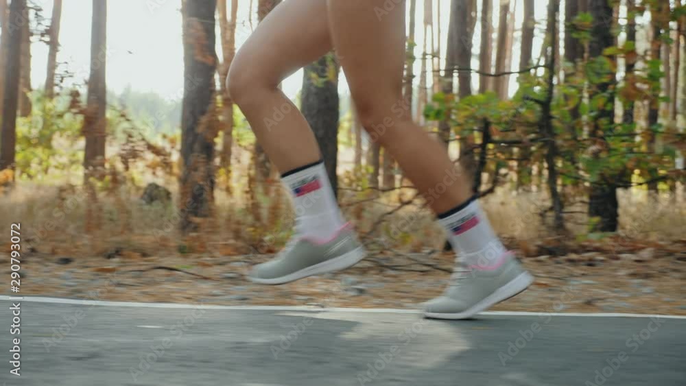 Morning jogging through the forest, only legs closeup. Girl runs along the road in a pine forest, slow-motion 4k video. Female jogging outdoors. US flag printed on the socks Morning jogging through the forest, only legs closeup. Girl runs along the road in a pine forest, slow-motion 4k video. Female jogging outdoors. US flag printed on the socks