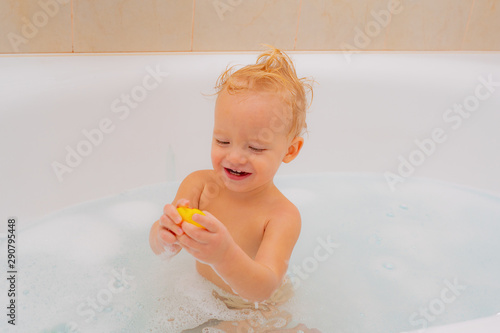 Smiling kid in bathroom. Funny baby playing with water and foam in a big kitchen sink. Funny cheerful toddler cleaning body in the bath.