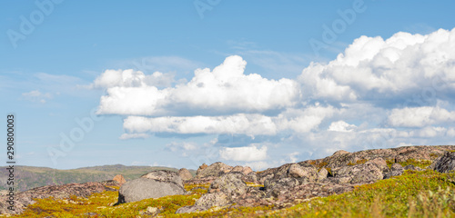 Huge rounded stones on backdrop of hills, small mountains and low Northern the sky. Over stones, hills and grass smoothly move huge white clouds