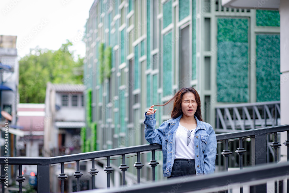 Portrait of Hipster Asian woman in white t-shirt, jean jacket and black trousers with beautiful modern building in background Portrait of Hipster Asian woman in white t-shirt, jean jacket and black trousers with beautiful modern building in background