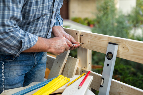 Adult carpenter craftsman with screwdriver screw the screw to fix the boards of a wooden fence. Housework do it yourself. Stock photography.