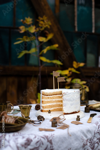 beautiful outdoor still life with naked biscuit multi layered naked cake with white cream stands on table with beige tablecloth  brass vintage plates  cups in autumn garden