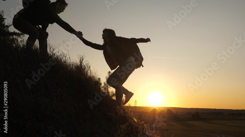 A male traveler holds out his hand to a female traveler climbing a hilltop. Tourists climb the mountain in the sunset, holding hands. teamwork of business people. Happy family on vacation.