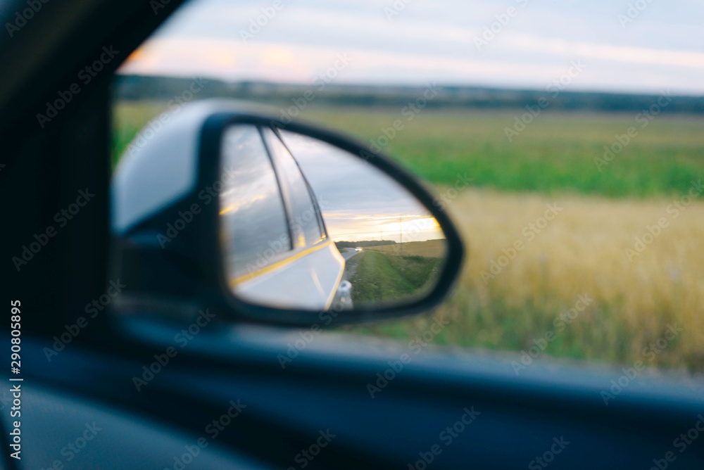 Reflection of the route in the side mirror of the car. Sunset. Summer. Travelling by car. Reflection of the route in the side mirror of the car. Sunset. Summer. Travelling by car.