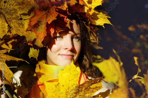 Portrait of a young brunette girl in a wreath of autumn maple leaves on yellow and red foliage