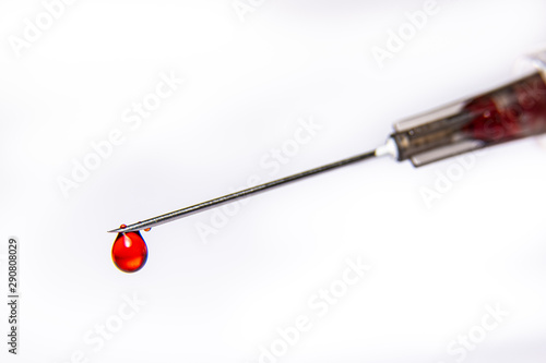 A syringe dripping a red blood like fluid isolated against a pure white background