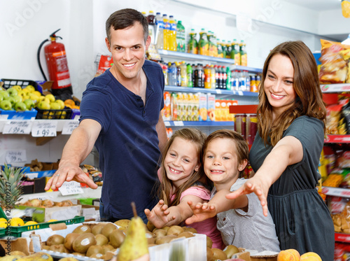 Smiling family with kids points to fresh delicious fruits in supermarket