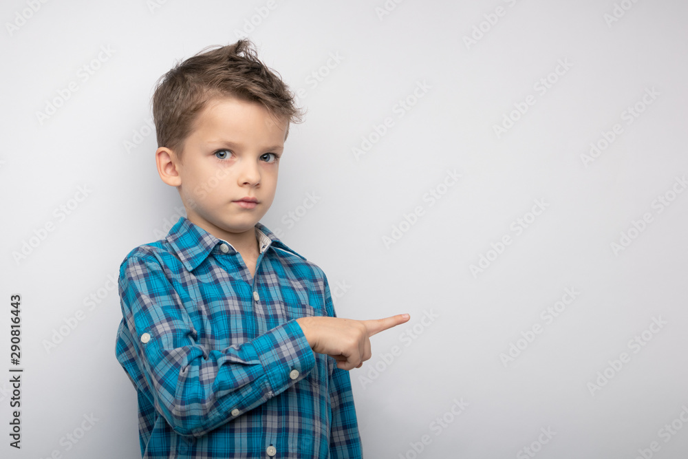childhood, gesture and people concept-portrait of smiling little boy in plaid shirt pointing finger on grey background