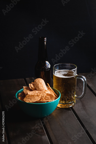 Set of french fries on the wooden table with glass of beer and black background