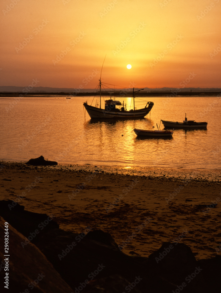 Tres barcas pesqueras amarradas en puerto de un delta de río en un atardecer anaranjado y agua en calma