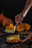 Zucchini pie with baked pumpkin on a spatula in women's hands in the kitchen, on a dark wooden background close-up with copy space.