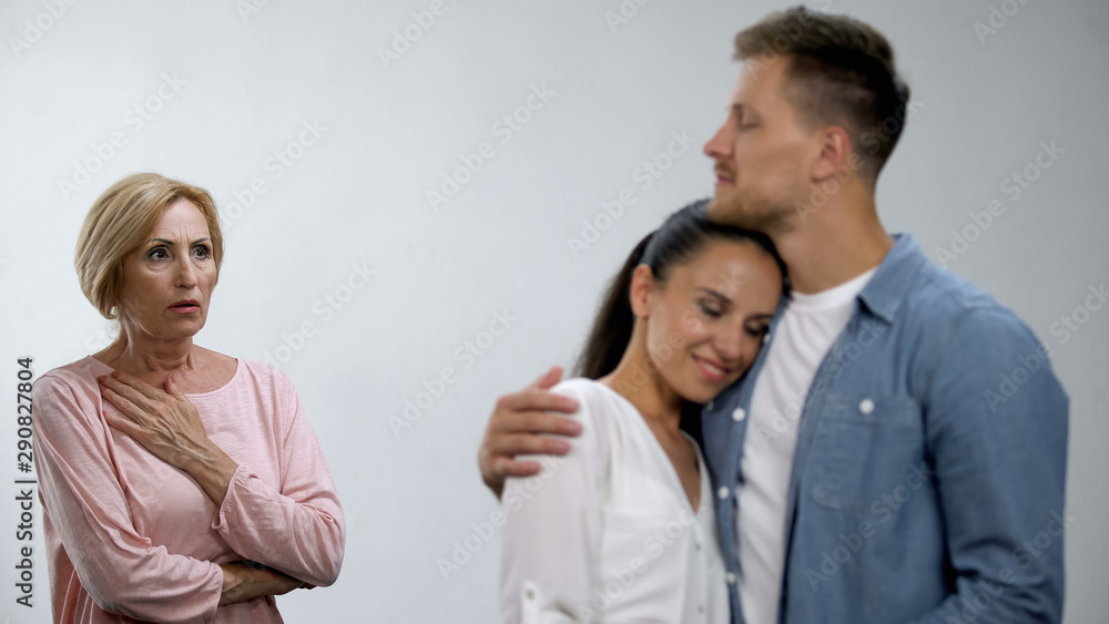 Worried mother-in-law looking at son hugging wife, unwanted relationship Worried mother-in-law looking at son hugging wife, unwanted relationship
