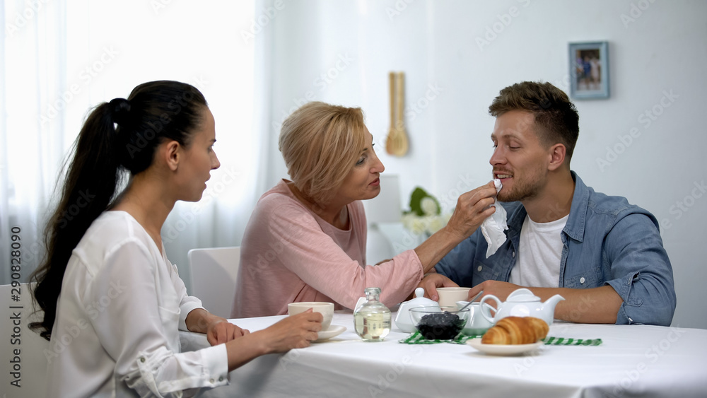 Shocked wife looking at mother-in-law wiping husbands mouth during tee party