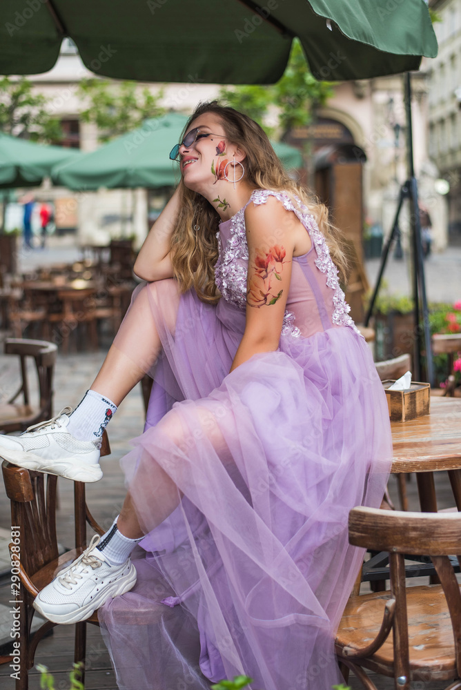 Naklejka premium Portrait of young gil wearing dress and sneakers and socks. tattoes over her arms and face. Close up. City walk.
