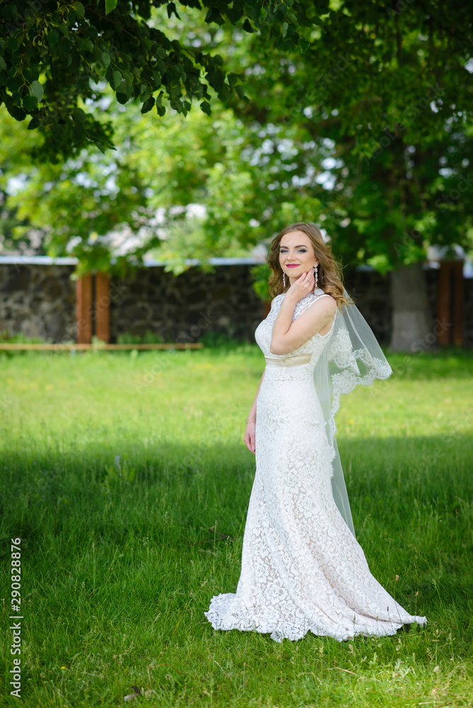 Full length photo of conceived blonde bride in a white dress in the summer park
