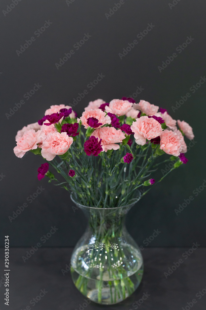 A large bouquet of red and pink carnations in a transparent glass vase on a dark background