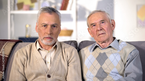 Depressed old men sitting on sofa looking camera, social insecurity, poverty