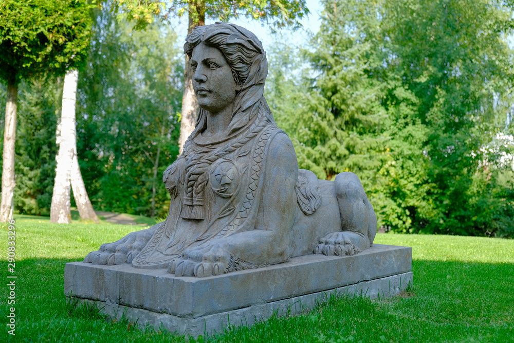 Stone ancient sphinx sculpture in a park on a green lawn.