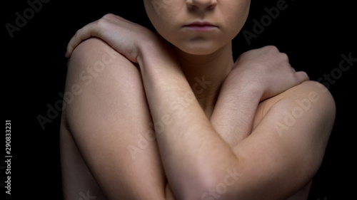 Naked woman hiding body with hands, black background, human trafficking concept