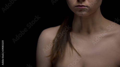 Naked woman standing against black background, sexual harassment concept