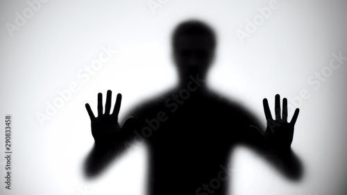 Shadow of trapped man touching glass wall, room escape concept, close-up photo