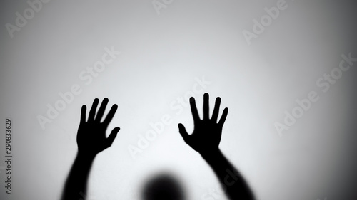 Silhouette of hands sliding down glass wall, person dying, crime scene, horror photo