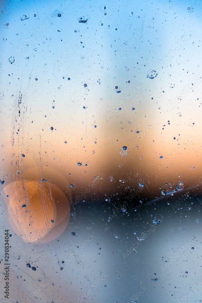 Abstract water drops on a port hole ship window over blur background at sunset.
