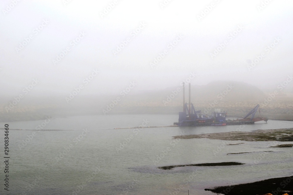 sand excavating and dredging ship ( dredger ship , dredger ) machine removing sand from lake , river  with misty weather