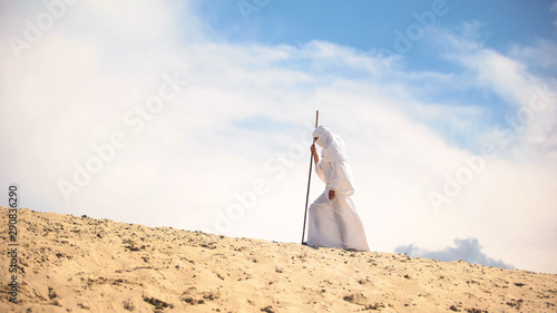 Tired Bedouin with staff walking in hot desert, climate change, global warming
