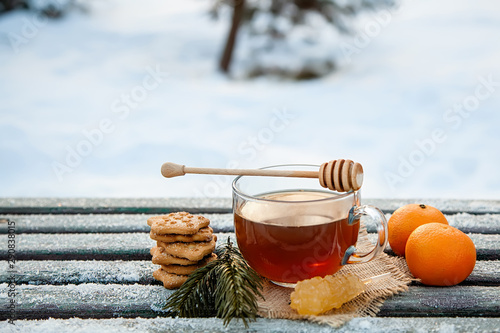 Cup of hot tea witn honey , tangerines and cookies in the winter forest. the concept of Christmas still life