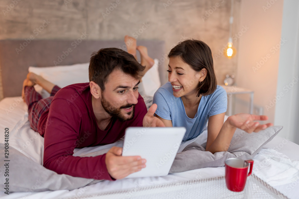 Couple in bed drinking coffee and using tablet computer Couple in bed drinking coffee and using tablet computer