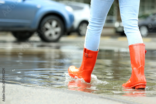 Woman with rubber boots in puddle, closeup. Rainy weather