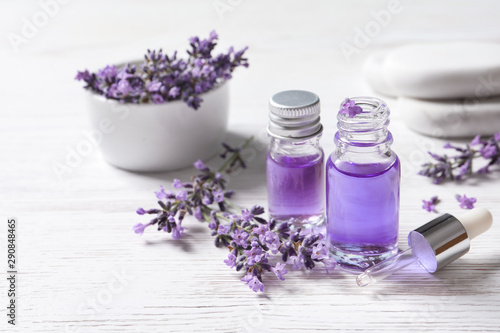 Glass bottles of natural cosmetic oil and lavender flowers on white wooden table