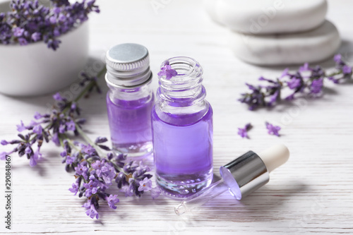 Glass bottles of natural cosmetic oil and lavender flowers on white wooden table