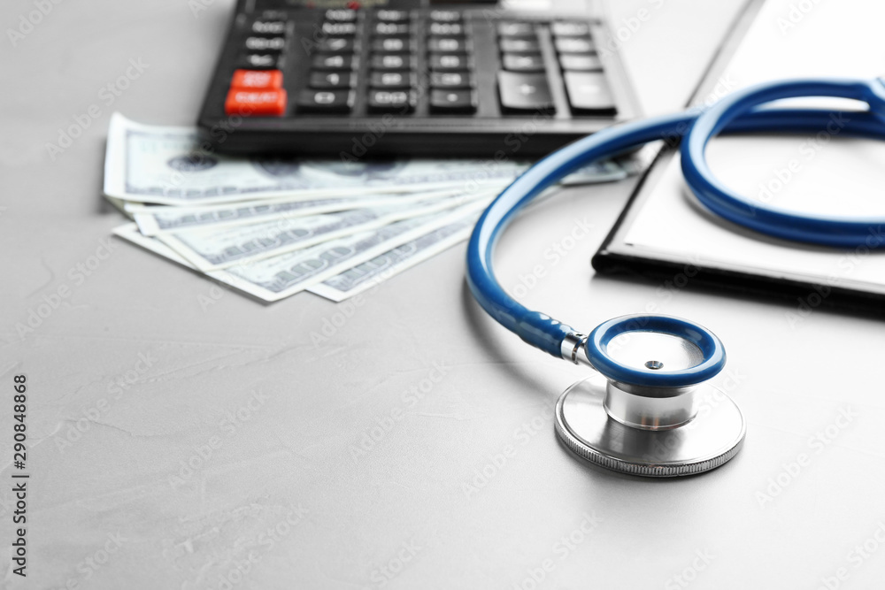 Stethoscope with money, clipboard and calculator on grey table, closeup. Medical insurance concept Stethoscope with money, clipboard and calculator on grey table, closeup. Medical insurance concept