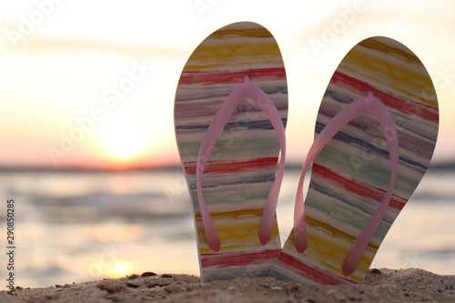 Stylish flip flops on sand near sea  closeup. Beach accessories